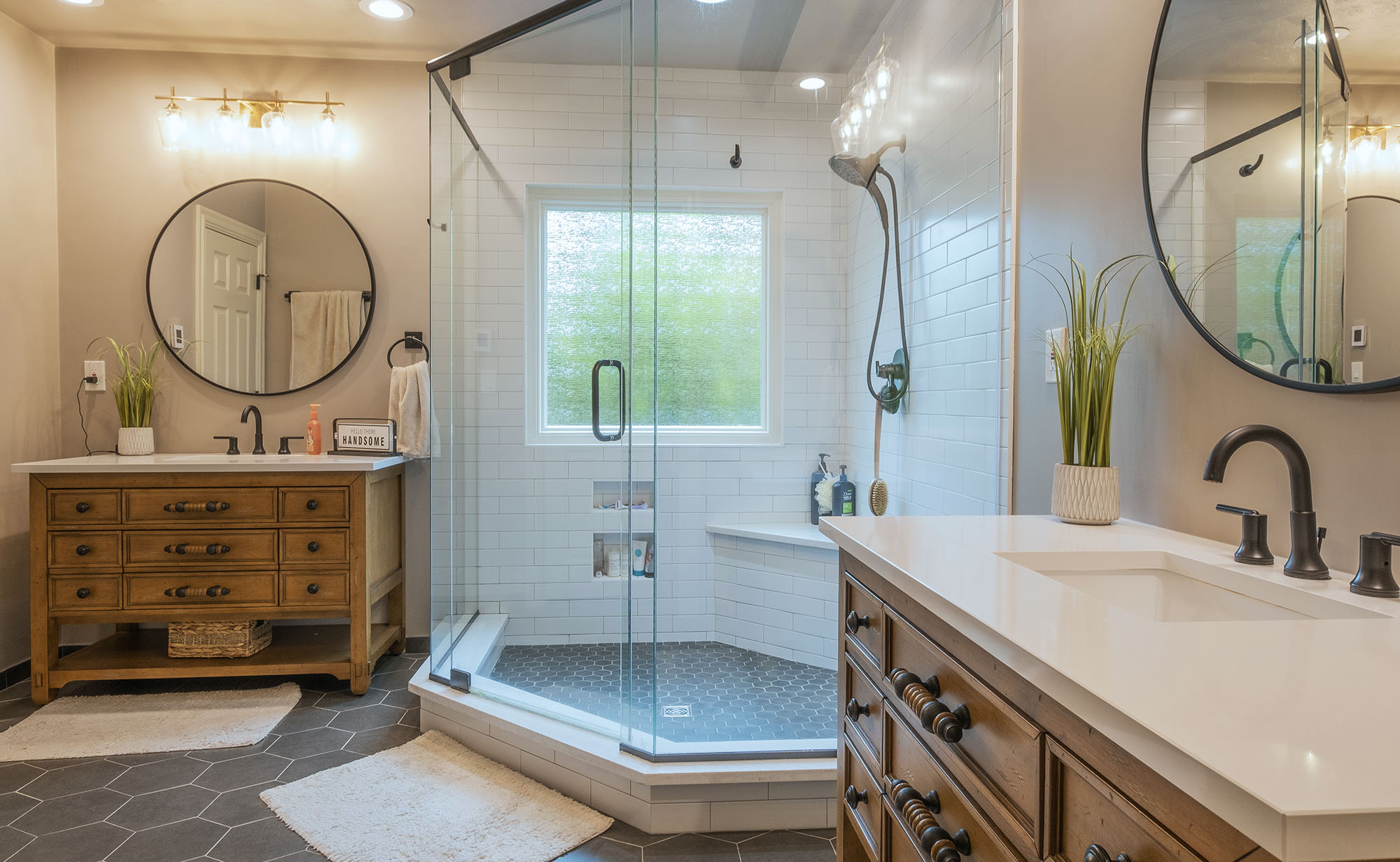 Large walk-in corner shower with bench seating, glass shower doors with white subway tile. Two large furniture styled vanities and octagonal tiled floor.