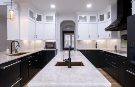 remodeled kitchen with black lower cabinets and white uppers. all black fixtures and a white natural stone countertop.